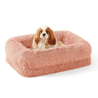 Dog lying on a fluffy pink pet bed against a white background